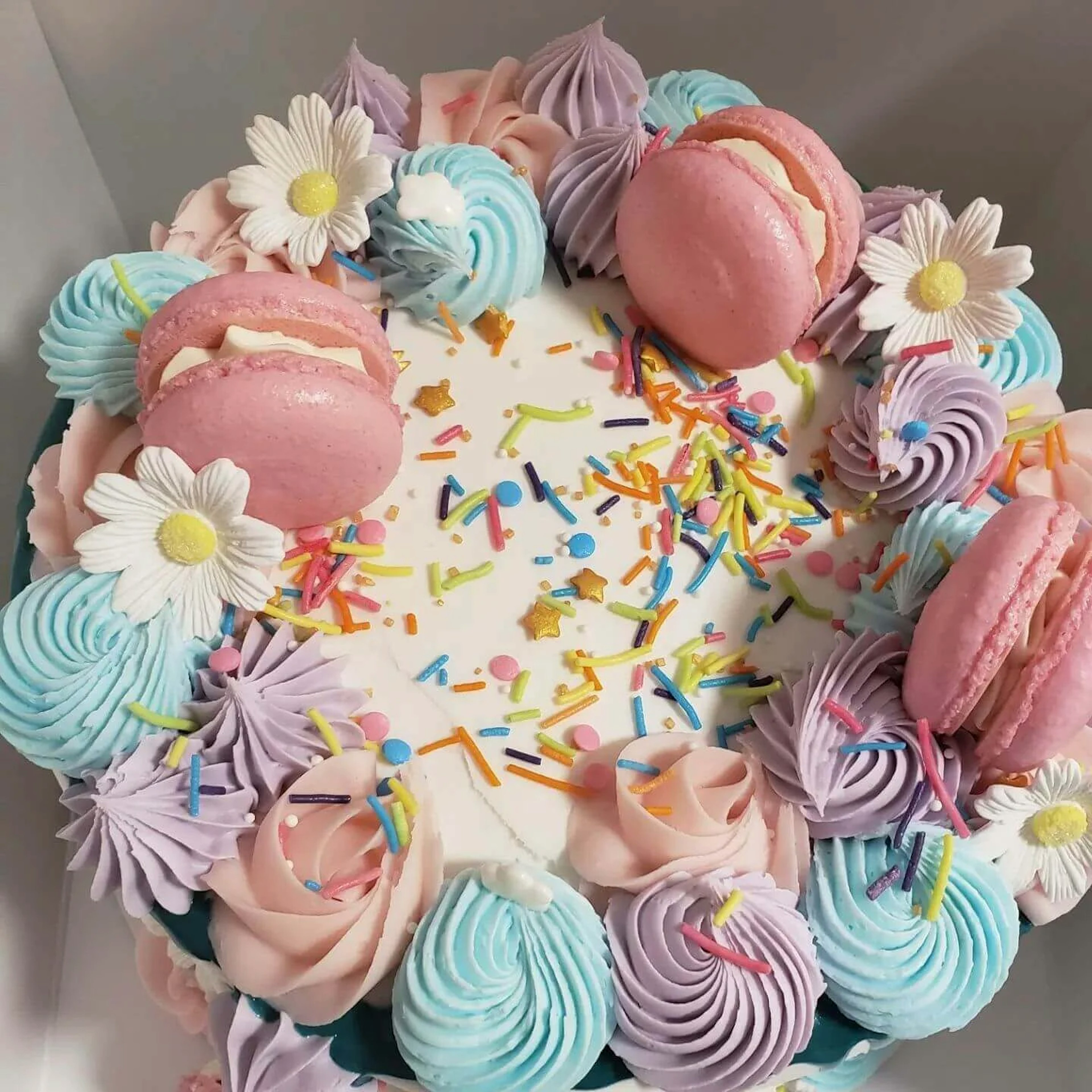 A teal and pink cake with macaroons on top. 