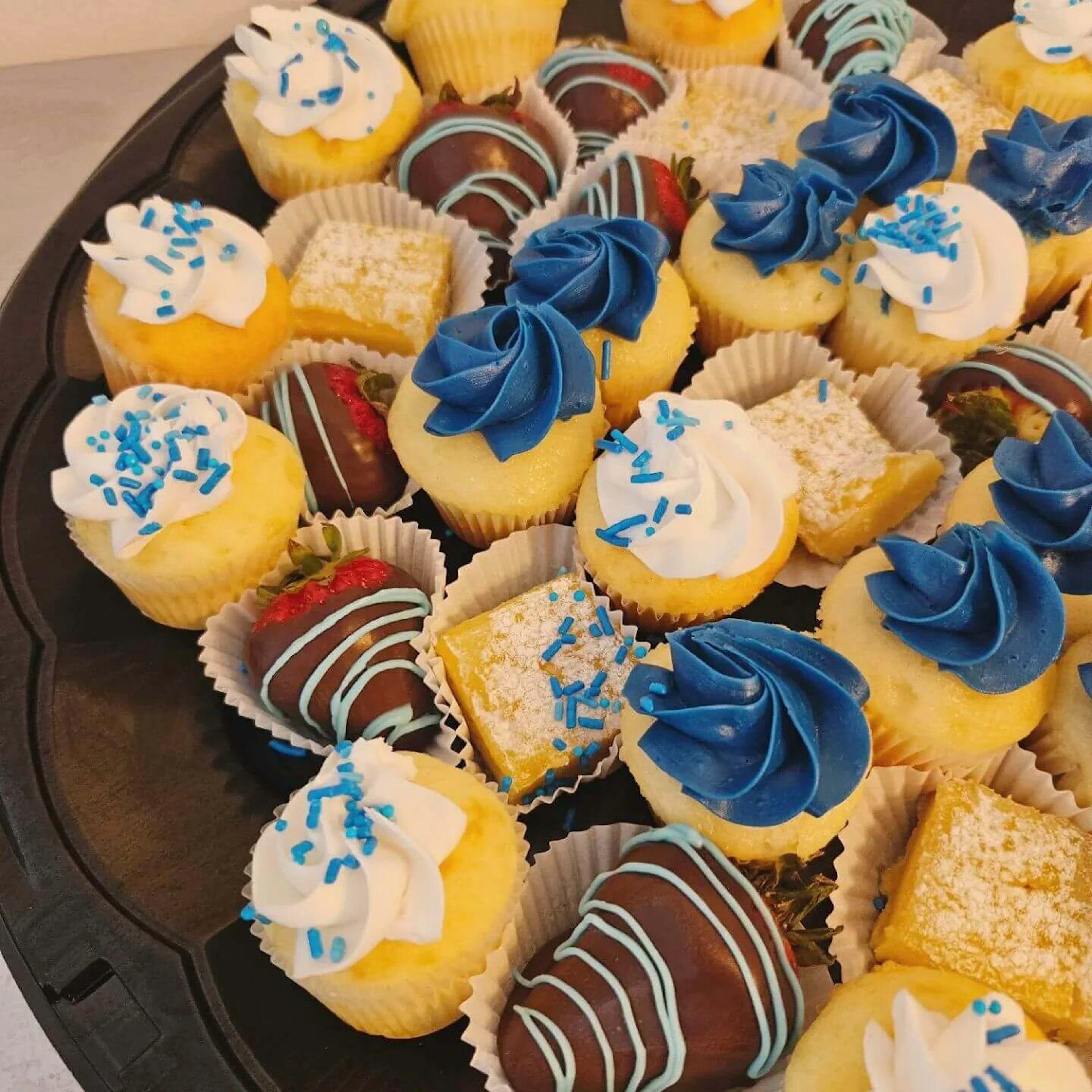 A tray of small cakes with blue and white frosting.